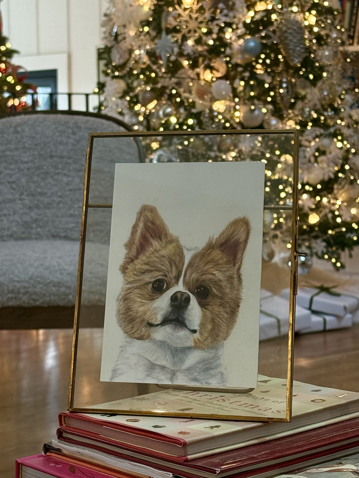 Framed drawn portrait of a small brown and white dog displayed in front of a Christmas tree